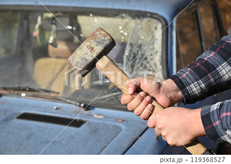A man is clutching a hammer in front of a bright blue car 119368527
