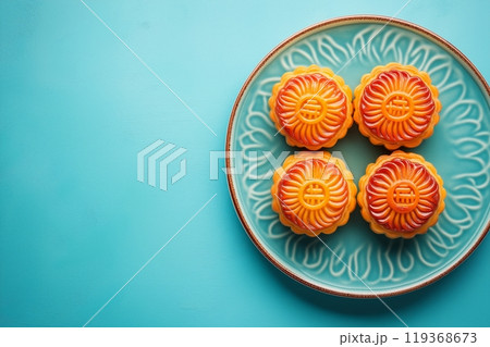 Four bright orange mooncakes with intricate designs on a teal ceramic plate, set on a teal background 119368673
