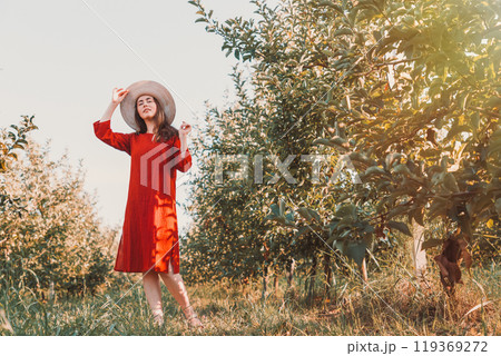 Portrait of a woman in the garden. A young and beautiful woman in a red dress and hat coquettishly takes off her hat. Copy space Portrait of a woman in the garden. A young and beautiful woman in a red dress and hat coquettishly takes off her hat. Copy space 119369272