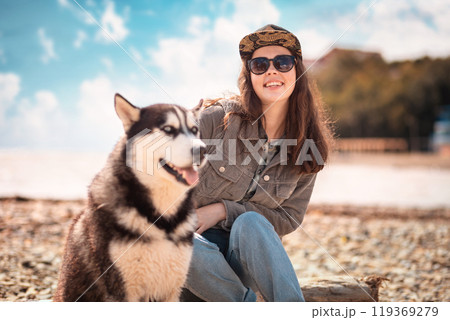 Portrait of a young happy woman and a husky dog. In the background, the beach, the sea and the cloudy sky. Concept of care and protection of pets 119369279