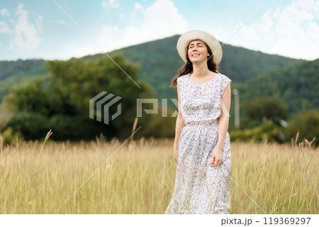 Summertime. Happy young woman in a straw hat and dress is walking in a meadow. The concept of psychology 119369297