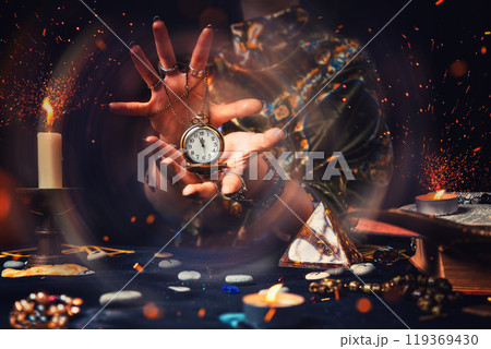 The fortune teller holds a watch on a chain in her hands, and works magic on them. Magic aura. The concept of divination, astrology and predicting the future 119369430