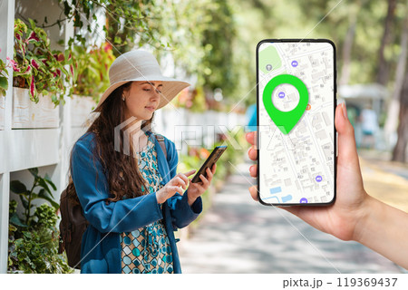 A females hand holds a smartphone with an online map app and a marked destination. In the background, a woman uses a phone. Concept of online navigation and modern technologies 119369437