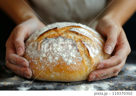 A golden, flour dusted loaf of bread held in hands, showing its fluffy and crisp texture 119370302