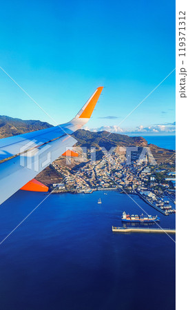 View from the airplane window on the wing and the island of Madeira, Portugal. Concept of air travel to Madeira to exotic countries View from the airplane window on the wing and the island of Madeira, Portugal. Concept of air travel to Madeira to exotic countries 119371312