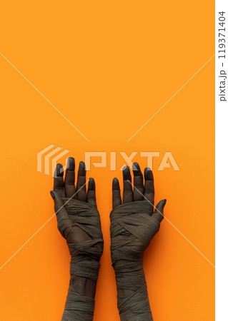 Two hands, wrapped in dark bandages, gesture openly against an orange backdrop 119371404