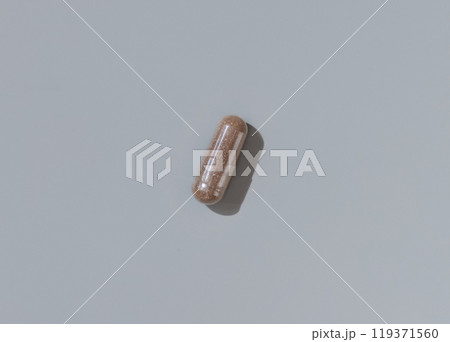 Brown Medical capsule on grey top view, hard shadows. Taking dietary supplements Brown Medical capsule on grey top view, hard shadows. Taking dietary supplements 119371560