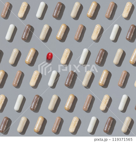 Patern of beige medical capsules with one red on grey top view, hard shadows. Herbal dietary supplements Patern of beige medical capsules with one red on grey top view, hard shadows. Herbal dietary supplements 119371565