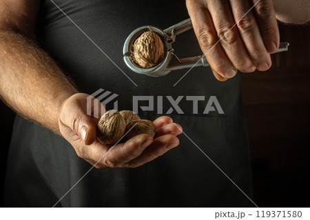Chef peeling walnuts with his hands and a nutcracker. Close-up of cook hands with a nutcracker while working Chef peeling walnuts with his hands and a nutcracker. Close-up of cook hands with a nutcracker while working 119371580