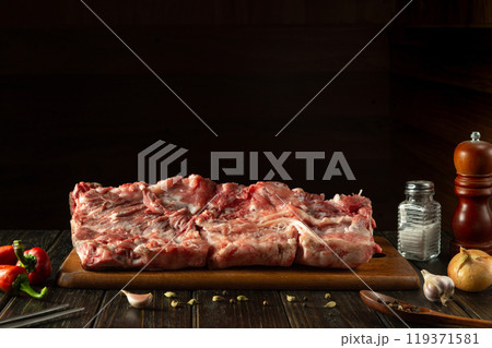 Large piece of meat on a cutting kitchen board. Raw ribs on the kitchen table. Space on a black background for a recipe or menu Large piece of meat on a cutting kitchen board. Raw ribs on the kitchen table. Space on a black background for a recipe or menu 119371581