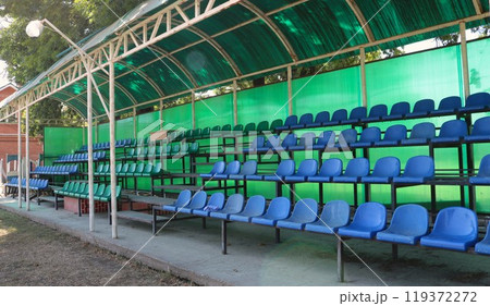 blue and green plastic chairs under a green canopy, a fragment of an open-air spectator stand without visitors, places for watching horse races at a provincial hippodrome blue and green plastic chairs under a green canopy, a fragment of an open-air spectator stand without visitors, places for watching horse races at a provincial hippodrome 119372272