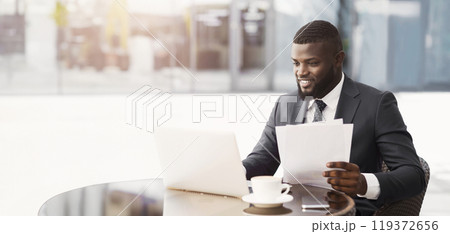 Confident African Entrepreneur Sitting At Laptop Working With Papers Sitting In Cafe Outside. Business Lifestyle. Free Space 119372656
