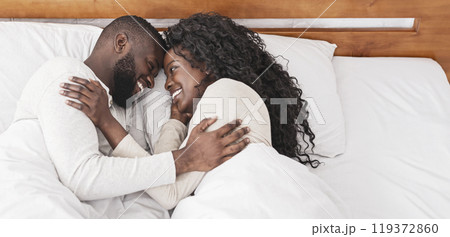 Lovely morning. Black millennial couple cuddling in bed at home, resting, and enjoying weekend together 119372860
