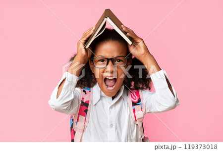 Angry School Girl Shouting Holding Book On Head Tired Of Quarantine Homework Standing Over Yellow Background. Studio Shot 119373018