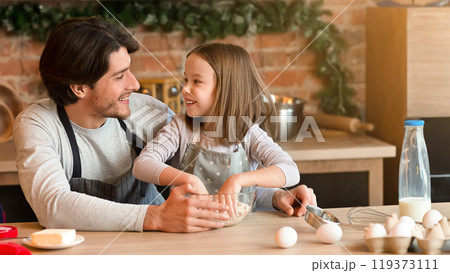 Cute little girl and her father making dough together, having fun at kitchen, looking at each other with love and care while preparing pastry 119373111