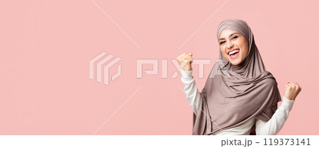 Yes. Happy muslim woman in hijab rejoicing success, raising hands and exclaiming with winner face expression 119373141