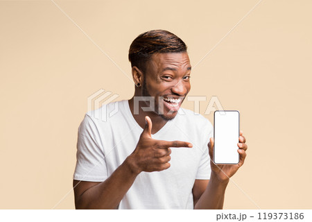 Afro Man Pointing Finger At Smartphone With Blank Screen In Hand Smiling At Camera Standing Over Yellow Background. Mockup 119373186
