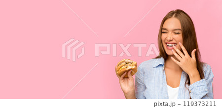 Fast Food. Happy Girl Eating Burger Laughing Posing On Yellow Studio Background. Panorama, Copy Space Fast Food. Happy Girl Eating Burger Laughing Posing On Yellow Studio Background. Panorama, Copy Space 119373211