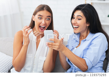 Happy Girl Showing Message On Phone To Friend Excited About Something Sitting On Sofa Indoor. Selective Focus Happy Girl Showing Message On Phone To Friend Excited About Something Sitting On Sofa Indoor. Selective Focus 119373293