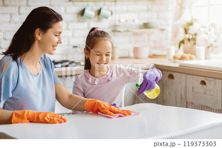 A mother and her young daughter are cleaning their kitchen table together. TThey both have happy expressions on their faces, suggesting that they are enjoying their time together. 119373303