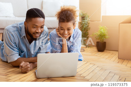 Moving Concept. Black Spouses Using Laptop Watching Movie Lying On Floor In New Apartment. Selective Focus, Free Space Moving Concept. Black Spouses Using Laptop Watching Movie Lying On Floor In New Apartment. Selective Focus, Free Space 119373375