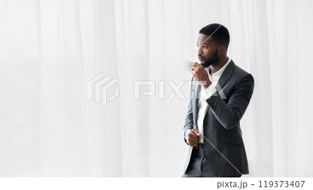 Serious african american businessman drinking coffee near window in office after hard day at work, copy space 119373407