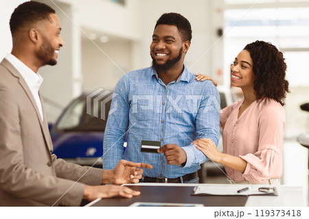 Afro Couple Buying Car Giving Seller Credit Card Standing In Auto Dealership Office. Selective Focus 119373418