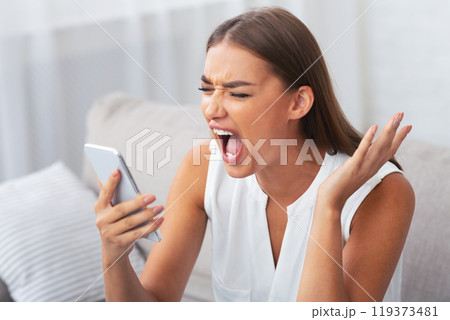 Angry Young Woman Shouting On Cellphone Having Phone Quarrel With Boyfriend Sitting On Sofa At Home. Selective Focus Angry Young Woman Shouting On Cellphone Having Phone Quarrel With Boyfriend Sitting On Sofa At Home. Selective Focus 119373481