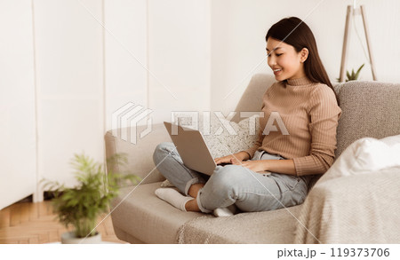 Teen Girl Surfing Internet on Laptop Computer, Sitting on Sofa with Crossed Legs, Free Space Teen Girl Surfing Internet on Laptop Computer, Sitting on Sofa with Crossed Legs, Free Space 119373706