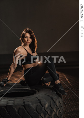 A vibrant and energetic dynamic fitness pose showcases a determined female athlete as she engages with a tire in an intense workout environment where she embodies grace, power, and motivation A vibrant and energetic dynamic fitness pose showcases a determined female athlete as she engages with a tire in an intense workout environment where she embodies grace, power, and motivation 119373707