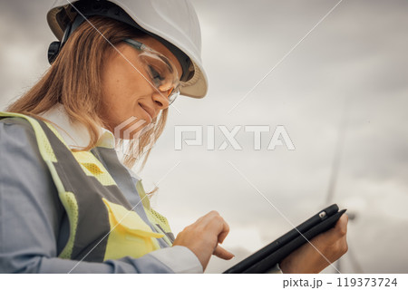At a busy construction site, a skilled female worker uses a tablet to communicate and collaborate with her team, enhancing efficiency and productivity in various tasks and operations At a busy construction site, a skilled female worker uses a tablet to communicate and collaborate with her team, enhancing efficiency and productivity in various tasks and operations 119373724
