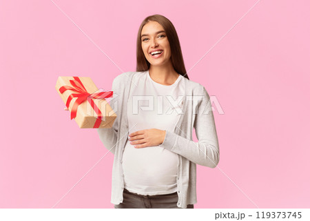 Baby Shower Concept. Happy Pregnant Lady Holding Wrapped Gift Box Looking At Camera Standing Over White Background. Studio Shot 119373745