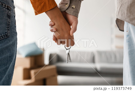 Closeup of young couple holding hands and new house key, moving in together. Unrecognizable boyfriend and girlfriend relocating to their own property, cropped view. Mortgage, real estate concept Closeup of young couple holding hands and new house key, moving in together. Unrecognizable boyfriend and girlfriend relocating to their own property, cropped view. Mortgage, real estate concept 119373749
