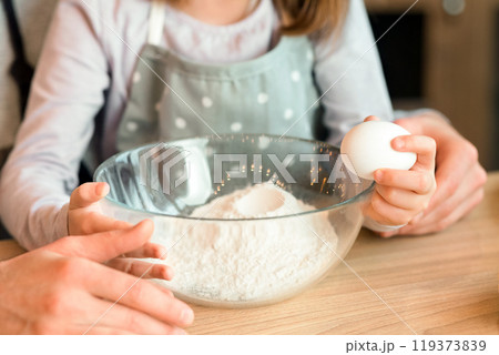 Closeup of little girl cracking egg to bowl, helping father with cooking pastry, enjoying baking at home, cropped image 119373839