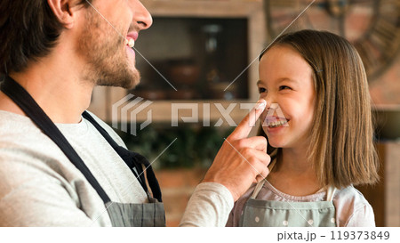 Cheerful Little Girl And Her Young Dad Having Fun In Kitchen Together, Fooling While Baking Pastry At Home, Loving Father Playfully Coloring Daughter's Nose With Flour And Smiling, Closeup Portrait 119373849