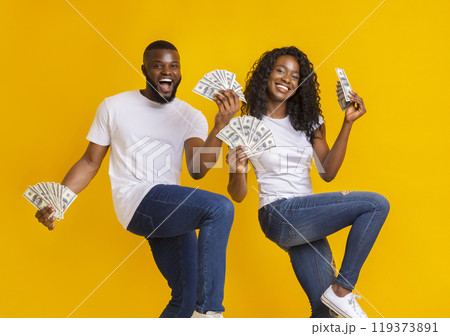 African american cheerful couple dancing with money in their hands, lifting legs up 119373891