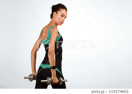 Determined Afro Girl Working Out With Dumbbells On Yellow Studio Background. Strength Exercises Concept. Free Space Determined Afro Girl Working Out With Dumbbells On Yellow Studio Background. Strength Exercises Concept. Free Space 119374601
