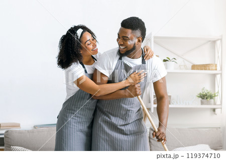 Happy black couple doing household chores together, mopping floor and hugging, spring-cleaning their apartment Happy black couple doing household chores together, mopping floor and hugging, spring-cleaning their apartment 119374710