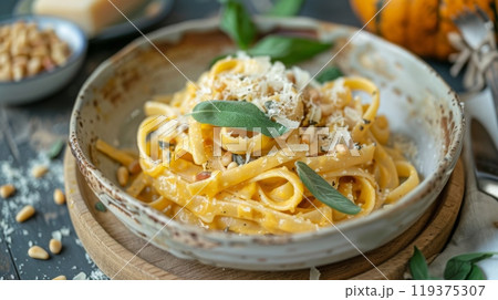Delicious pasta tossed in a creamy pumpkin sauce, garnished with fresh sage leaves and pine nuts, served in a rustic bowl. Delicious pasta tossed in a creamy pumpkin sauce, garnished with fresh sage leaves and pine nuts, served in a rustic bowl. 119375307