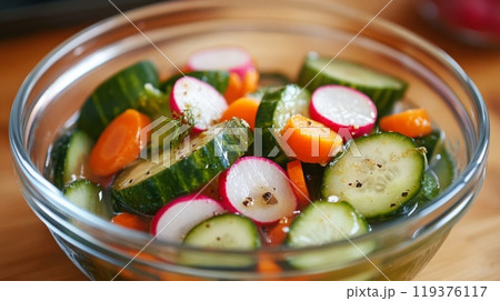 A colorful assortment of sliced cucumbers, radishes, and carrots tossed together, showcasing vibrant freshness. 119376117
