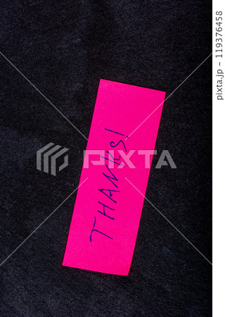 A pink sticky note displaying the word Thanks on a textured dark background, conveying gratitude and appreciation. 119376458