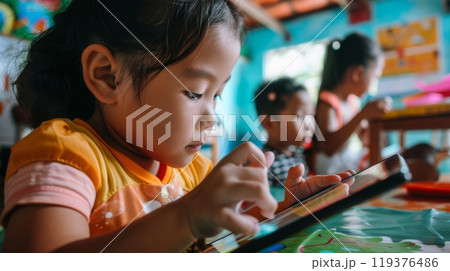 A child focuses intently on a tablet, participating in an educational activity within a vibrant classroom filled with artwork. A child focuses intently on a tablet, participating in an educational activity within a vibrant classroom filled with artwork. 119376486
