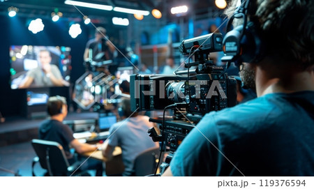 A cameraman films a scene on a studio set, with other crew members working in the background. 119376594