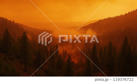 Thick smoke from a wildfire creates an eerie orange haze that blankets a mountainous forest, obscuring the trees and altering the natural landscape at sunset. 119376722