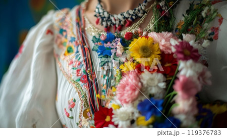 A person showcases a beautifully embroidered traditional outfit, decorated with vibrant flowers during a cultural event. 119376783