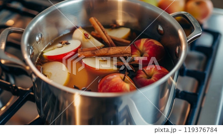Fresh apple slices, cinnamon sticks, and spices are simmering in a pot, creating a fragrant blend on the stovetop. 119376784
