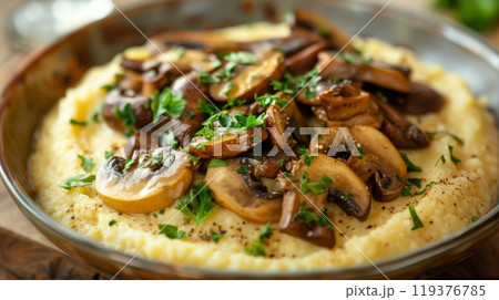 Creamy polenta topped with sauteed mushrooms and fresh parsley, served in a rustic bowl with herbs. 119376785