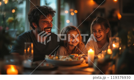 A father enjoys a heartwarming dinner with his two daughters, sharing laughter and stories while candles create a cozy atmosphere. The warm light enhances their joyful expressions. 119376930