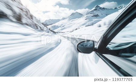 A car speeds along a snow-covered road surrounded by majestic mountains under a bright blue sky, capturing the essence of winter travel and adventure in a remote, scenic location. 119377705