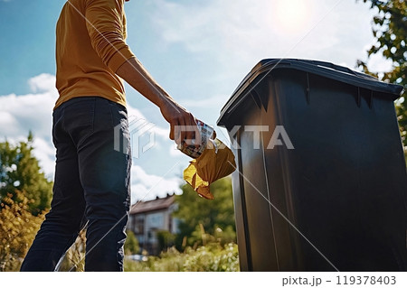 Man throwing away trash in garbage bin outside on sunny day 119378403